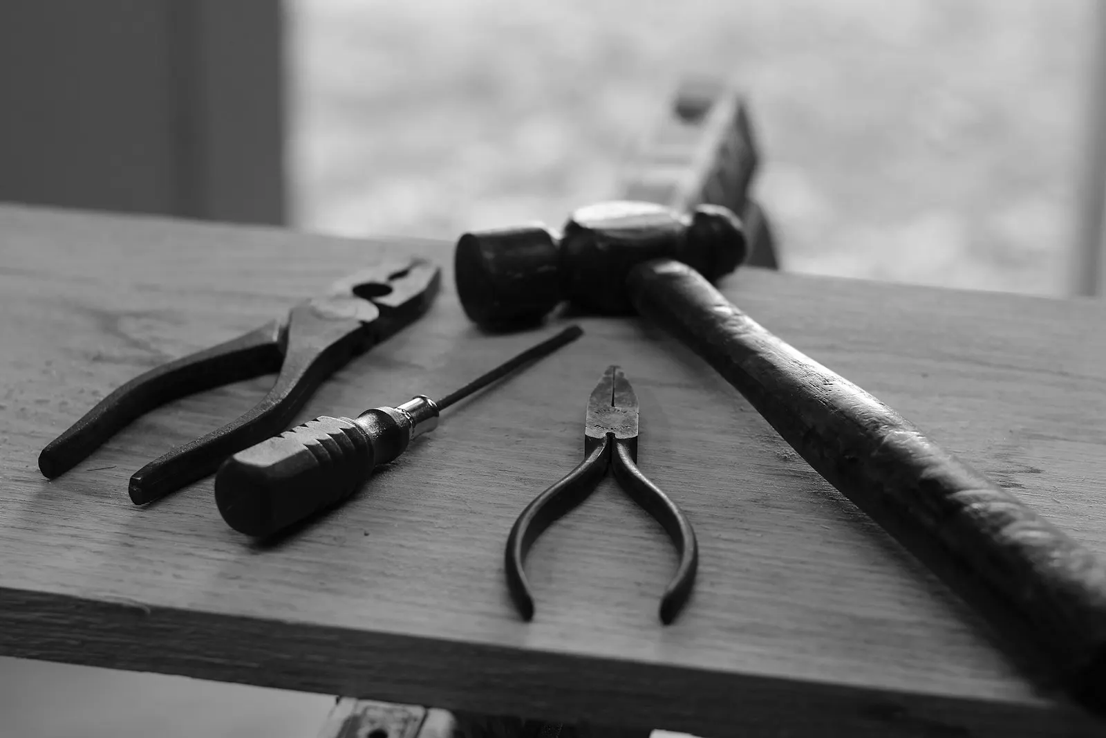 Four hand tools laid out on a wooden plank: pliers, a screwdriver, side cutters and a hammer