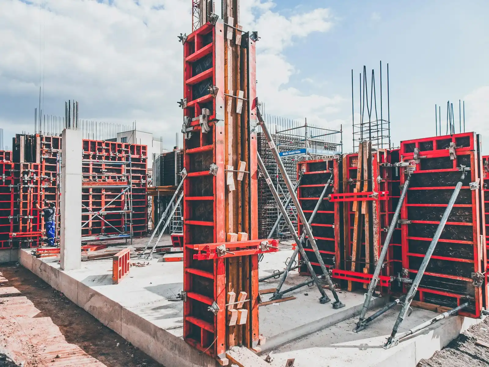 Red steel concrete formwork panels braced upright on a building site under a cloudy sky